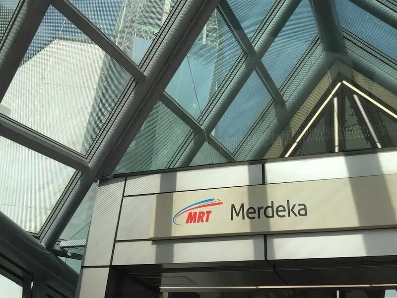 MRT Merdeka station signage beneath the glass canopy, with the Merdeka 118 tower visible through the roof